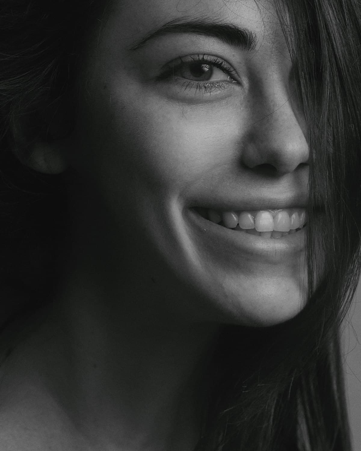 A close black-and-white portrait of a woman mid-smile, lit softly against a dark ground.